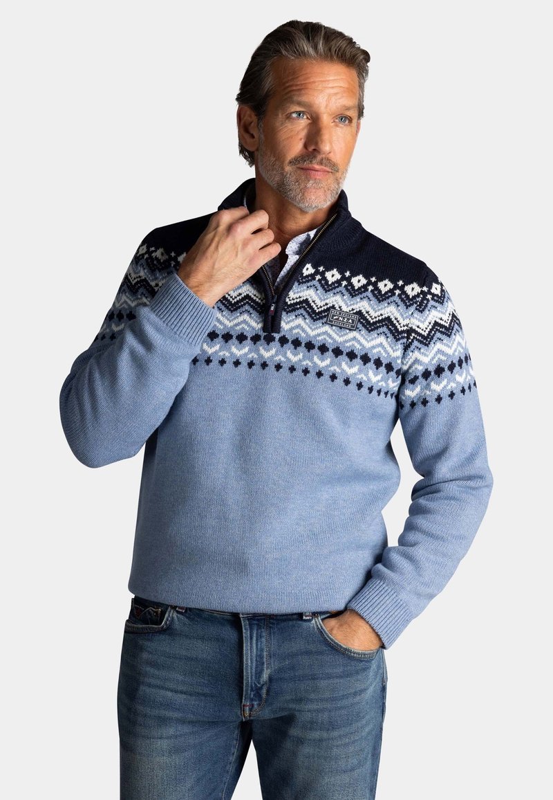 Lichtblauwe gebreide sweater met een marineblauwe kraag en een patroon op de schouders met witte en donkerblauwe geometrische ontwerpen. Met ritssluiting bij de hals.