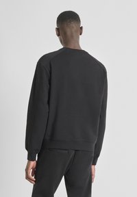 Sudadera negra de manga larga, con puños acanalados y cuello redondo. Confeccionada en una tela suave de textura lisa. Diseño minimalista.