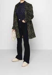 Kabát se zvířecím potiskem, námořnický pletený top, tmavé džíny s vysokým pasem a béžové platformové boty. Drží světle béžovou kabelku.