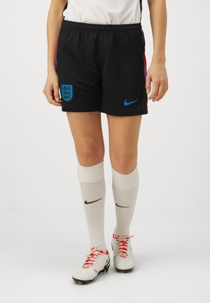 Pantalones cortos Nike negros con detalles azules, que presentan el escudo de Inglaterra. Media altas blancas con el logo negro de Nike, combinadas con botas blancas.
