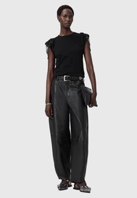 Czarna dopasowana bluzka z teksturowanymi zdobieniami na ramionach, w połączeniu z luźnymi czarnymi skórzanymi spodniami i płaskimi czarnymi butami. Trzyma czarną kopertówkę.