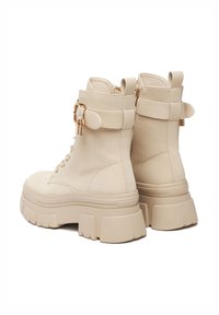 Beżowe skórzane botki na kostkę z masywną platformą, sznurowane z przodu, z bocznymi suwakiem oraz ozdobnymi klamrami przy kostce.