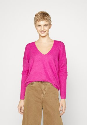 Bright pink knit sweater with a deep V-neck and long sleeves, paired with tan wide-leg pants. Soft texture and relaxed fit.