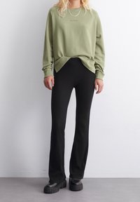 Olivově zelená mikina s volným střihem a žebrovanými manžetami, spojená s černými vysoko pasovými žebrovanými zvonovými kalhotami a masivními černými platformovými botami.