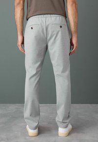 Gray sweatpants with a relaxed fit, elastic waistband, and two back patch pockets featuring button closures. Smooth fabric texture.