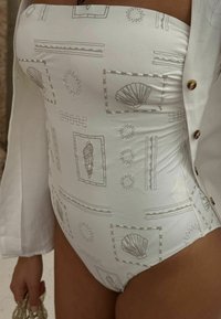 Bílý jednodílný plavky s texturovanou skořápkou a slunečními vzory v kontrastním světlém šedém vyšití. Má bezramenný design a hladký povrch.