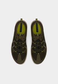 Ζευγάρι αθλητικών παπουτσιών σε ελιά χρώμα με πλεκτό ύφασμα, ελαστικές κορδόνια και μπεζ σόλες, σε θέα από πάνω σε λευκό φόντο.