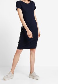 Navyblå kortärmad klänning i en figurnära design, med vita sidopaneler med text och ett fortfarande elastiskt tyg.