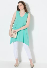 Una tunica senza maniche color verde menta con scollatura a V, abbinata a pantaloni bianchi fino alla caviglia con rifiniture in pizzo e scarpe slip-on con motivo.