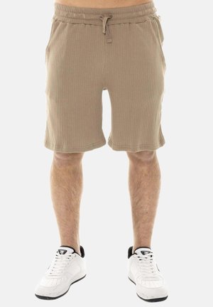 Pantaloncini beige a coste con coulisse indossati da una persona, abbinati a sneakers basse bianche con dettagli neri.