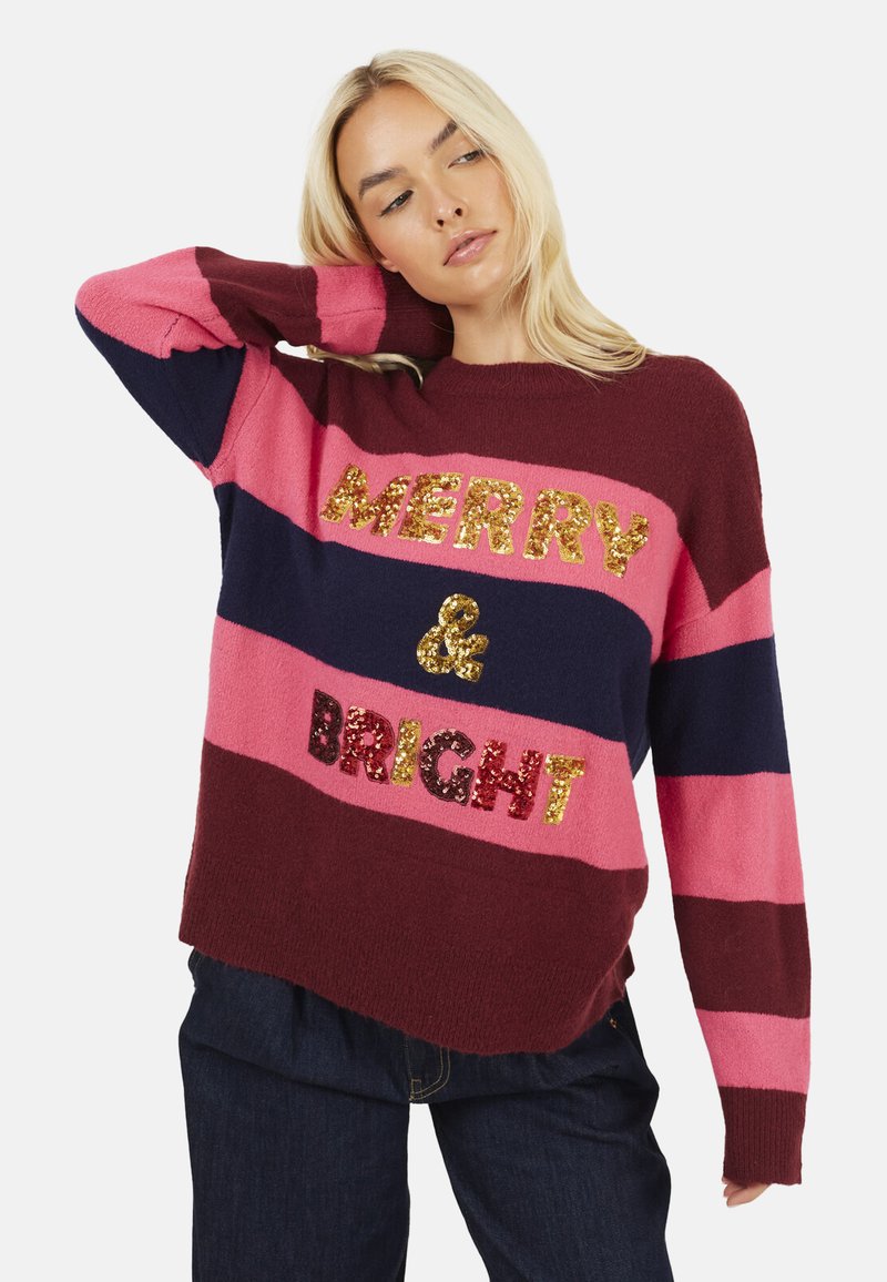 Maglione lavorato a maglia con strisce orizzontali in bordeaux, rosa e blu navy, con la scritta "MERRY & BRIGHT" in lettere di paillettes oro e rosse.