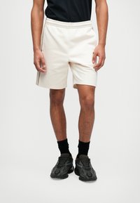 Crème-kleurige sportshorts met een elastische tailleband, zijzakken en een contrasterende zwarte streep langs de zijkanten.