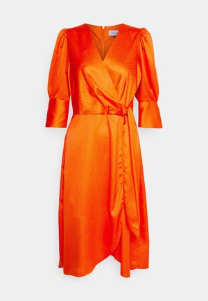 Oranje satijnen wikkeljurk met kleine zwarte polkadots, driekwart pofmouwen, V-hals en een zijstrik in de taille.