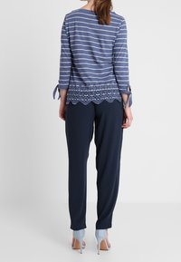 Blå och vit randig långärmad topp med spetsdetalj i botten, matchad med marinblå byxor och ljusblå klackar.