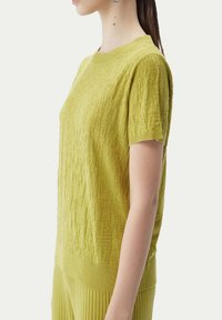Kortärmad, texturerad tröja i livlig limegrön färg. Har ett stickat mönster, ribbad halsringning och nederkant för en figurnära silhuett.
