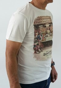 White cotton t-shirt with a colorful clown graphic, featuring text "Democracy in Action" and distressed edges around the print.