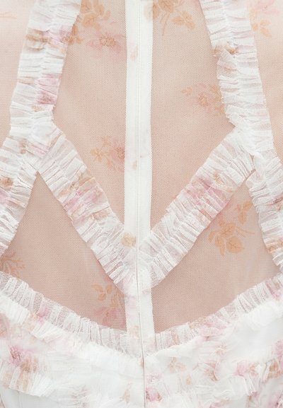 Ziedu tīkliņa kleita ar baltu volānu apdari, pārredzamu aizmuguri un maigu rozā ziedu rakstu uz bēša fona. Redzama rāvējslēdzēja detaļa.