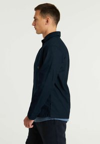 Chaqueta de hombre en azul marino hecha de una tela ligera y duradera. Cuenta con un cuello, bolsillos laterales y un corte recto para un ajuste relajado.