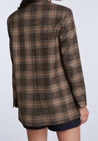 Brązowa i pomarańczowa kraciasta marynarka o długim, luźnym kroju, z usztywnionymi ramionami i czarnymi guzikami, wykonana z teksturowanej tkaniny.