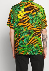 Kurzarmhemd mit schwarzem Grundton, lebhaften orangefarbenen Tigerstreifen und grüner tropischer Pflanzenwelt, akzentuiert durch gelbe Blumen.