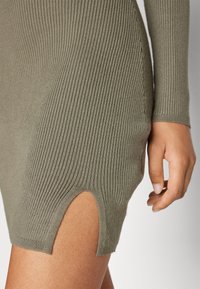 Khaki ribbad klänning med en figurnära design, långa ärmar och en sidospalt som framhäver ett texturerat, stretchigt tyg.