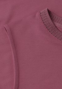 Tissu tricoté rose doux avec un gros plan sur un col en V présentant un motif texturé et perforé.