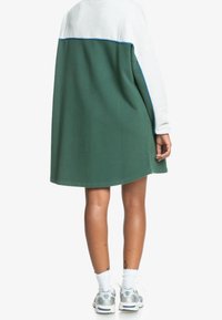 Vihreä ylisuuri college-mekko, jossa on harmaa yläosa, sinisiä yksityiskohtia, pitkät hihat ja kaareva helma, yhdistettynä tennareihin ja valkoisiin sukkiin.