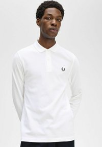 Polo bianco a maniche lunghe realizzato in un tessuto testurizzato, con colletto e un piccolo logo nero sul lato sinistro del petto.