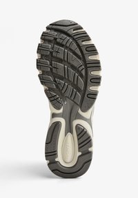 Čierna guma podošvy tenisky s textúrovanými vzormi, drážkami a krémovými akcentmi, s viditeľným logom a označením veľkosti.