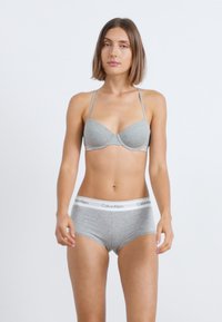 Šedá podprsenka s tenkými ramienkami a formovanými pohármi; zodpovedajúce šedé boxerky s bielym pásom s logom Calvin Klein. Hladká, elastická látka.