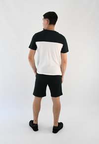 Conjunto atlético para hombre que presenta una camiseta de manga corta en bloque de colores negro y blanco, y pantalones cortos oscuros verdes. El material parece ser suave y elástico.