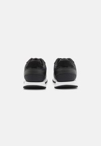 Scarpe da ginnastica nere con una tomaia texturizzata, tallone imbottito e suola bianca. Presentano un design elegante e un colletto imbottito per il comfort.