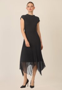 Vestido negro con un corsé ajustado y una falda asimétrica de gasa plisada y semitransparente. El material es una mezcla de tejidos sólidos y ligeros.