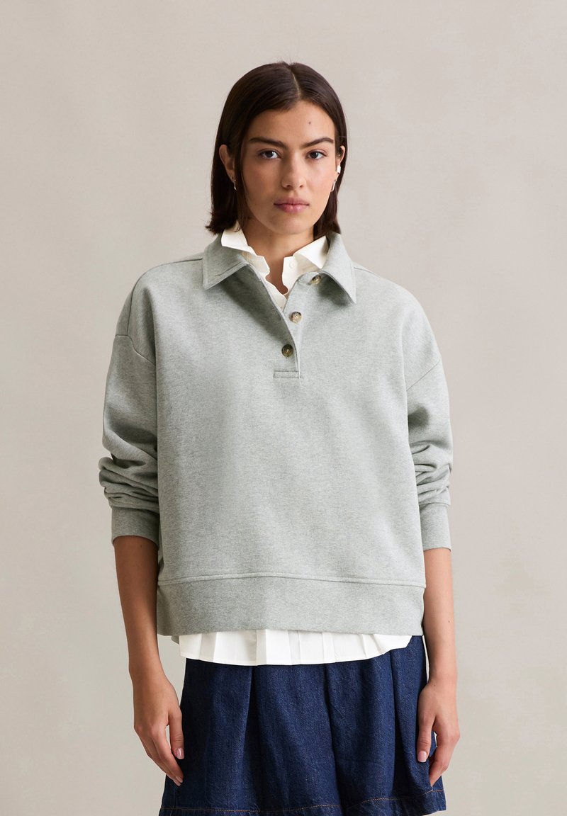 Gray sweatshirt with a collared neck, three buttons, and ribbed cuffs. Layered over a white shirt and paired with a denim skirt.