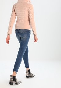 Beżowa pikowana kurtka z wysokim kołnierzem, niebieskie dopasowane dżinsy oraz czarno-białe botki w panterkę z grubym obcasem.