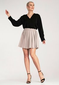 Czarna bluzka z długim rękawem i dekoltem w kształcie V, w zestawie z plisowaną spódnicą w kolorze beżowym o długości do kolan. Uzupełnieniem stroju są czarne sandały na szpilce.