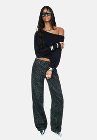 Pull noir à épaules dénudées, pantalon gris à imprimé léopard, accessoires en argent et escarpins argentés à bout pointu. Texture lisse et coupe ample.