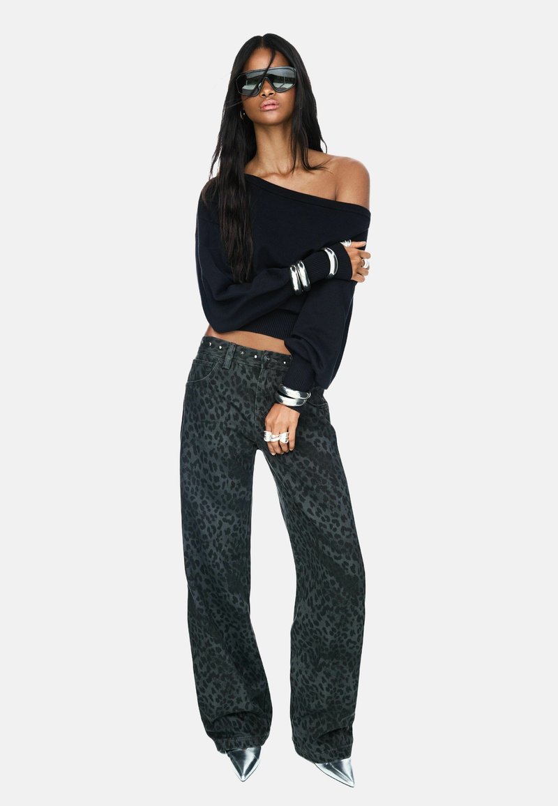 Pull noir à épaules dénudées, pantalon gris à imprimé léopard, accessoires en argent et escarpins argentés à bout pointu. Texture lisse et coupe ample.