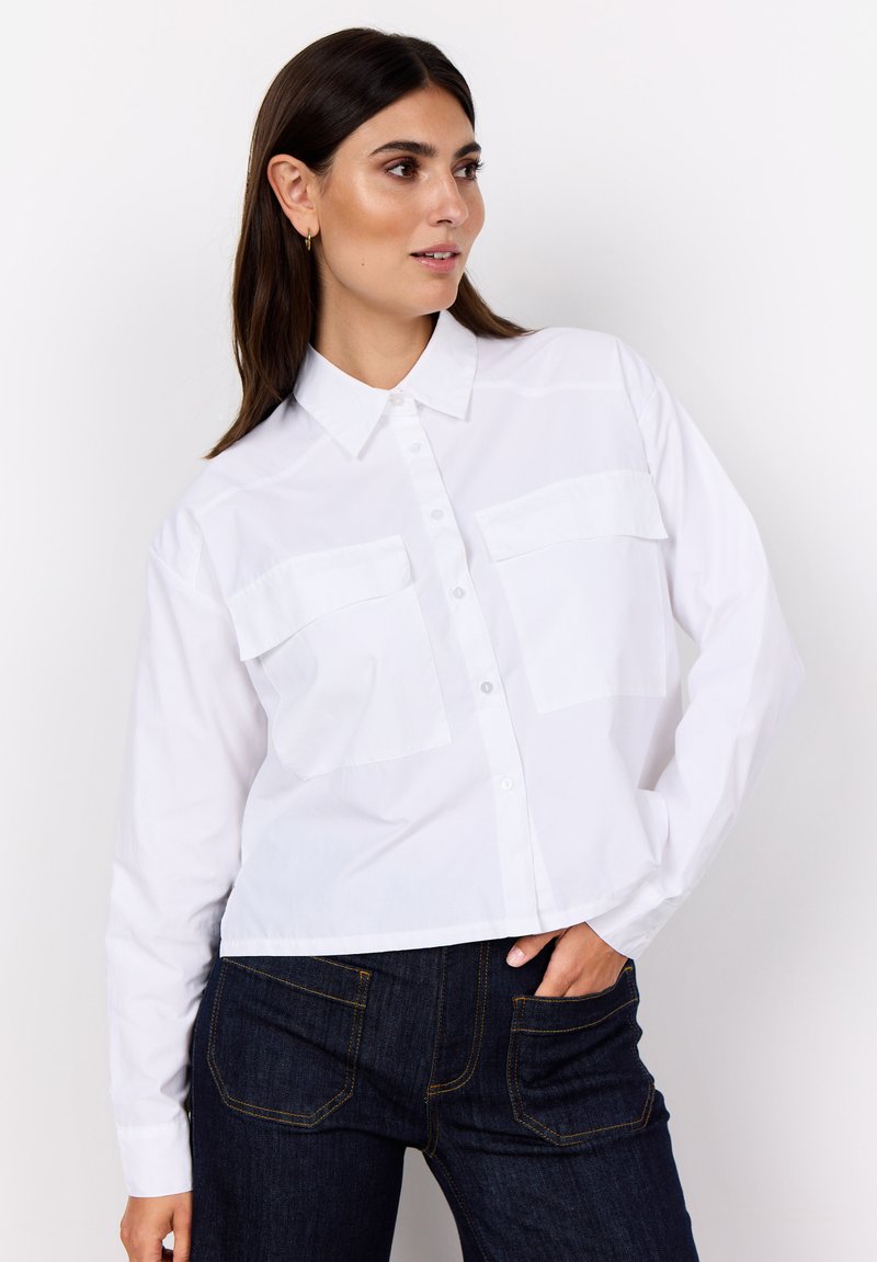 White button-up shirt with a collar, long sleeves, and two chest pockets. Material is smooth and lightweight; cropped design.