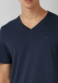 Granatowa koszulka typu v-neck z miękkiej bawełny. Posiada małe haftowane logo po lewej stronie. Gładka faktura, krótkie rękawy.
