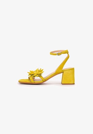 Yellow suede block heel sandal with ankle strap and buckle, open toe decorated with layered flower detail on front strap.