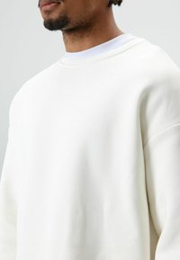Witte sweatshirt met een ontspannen pasvorm, gladde textuur en geribde halslijn. Voorzien van een ronde hals en schouders met doorgelopen naden.