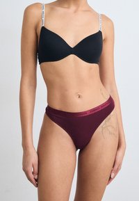 Black underwire bra with padded cups and logo-printed straps; maroon cotton thong with a contrasting waistband in bold red lettering.