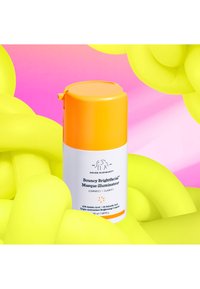 White cylindrical container with orange cap and label. Product name "Bouncy Brightfacial" in black. Surrounded by bright yellow squiggles.