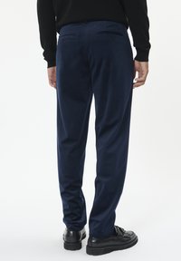 Mornarske hlače od mekog materijala, s opuštenim krojem, stražnjim džepovima s gumbima, u kombinaciji s crnim cipelama.