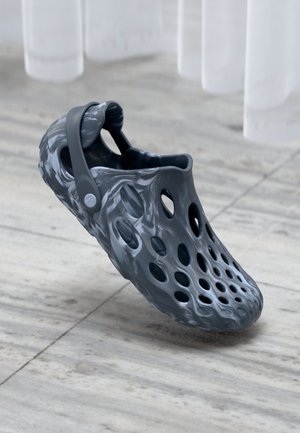 Sabots gris à motif avec plusieurs trous de ventilation, fabriqués en matériau flexible, dotés d'une bride arrière pour un ajustement sécurisé, sur un sol en marbre.