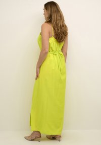 Rochie lungă, fără mâneci, dintr-un bumbac verde lime strălucitor, cu talie legată. Prezintă o fanta pe lateral și detalii din dantelă pe spate. Design simplu.