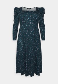 Robe vert foncé mi-longue avec manches bouffantes, encolure carrée et motif floral aux nuances de rose et de bleu. Tissu doux et texturé.