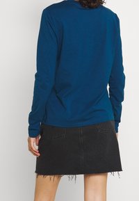 Long-sleeve blue cotton shirt paired with a black denim skirt featuring a frayed hem and back pockets. No visible branding details.