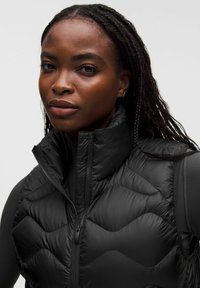 Musta tikattu untuvatakki, jossa korkea kaulus ja vetoketjukiinnitys. Kankaassa on sileä, kiiltävä pinta ja hienovarainen aaltoileva kuvio.